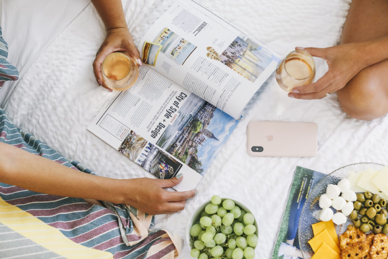 People reading magazine on hotel bed drinking Rose.